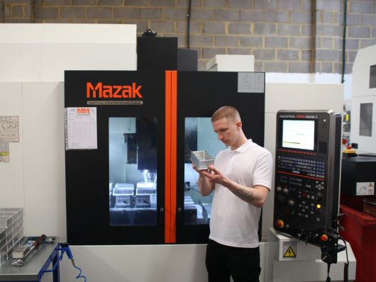 CNC engineer checking a part beside a Mazak machining centre
